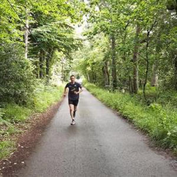 picture of Greg running on a path with woodlands on either side of him.